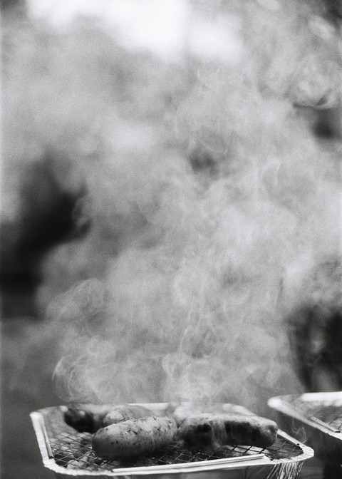 Sizzling sausages with smoke rising from a disposable barbeque
