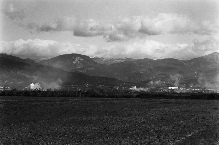 The mountain range of Taygetos viewed over farmers fields and smoke rising from buildings