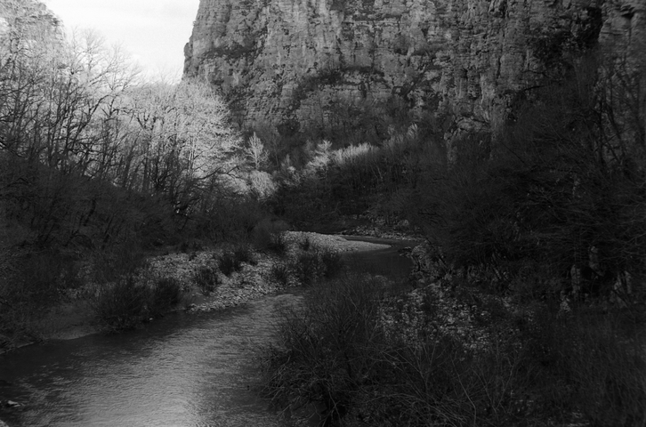 A view down the Voidomatis river from Kokkorou Bridge with sheer rock face and blossoming trees