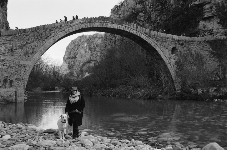 A woman and a white dog stood infront of the Kokkorou Bridge in Zagorohoria, Greece